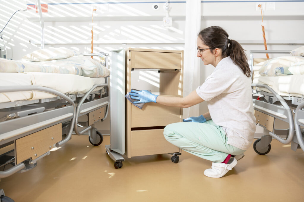 Im Patientenzimmer eines Spital wird das Nachtischmöbel mit einem Mikrofasertuch gereinigt